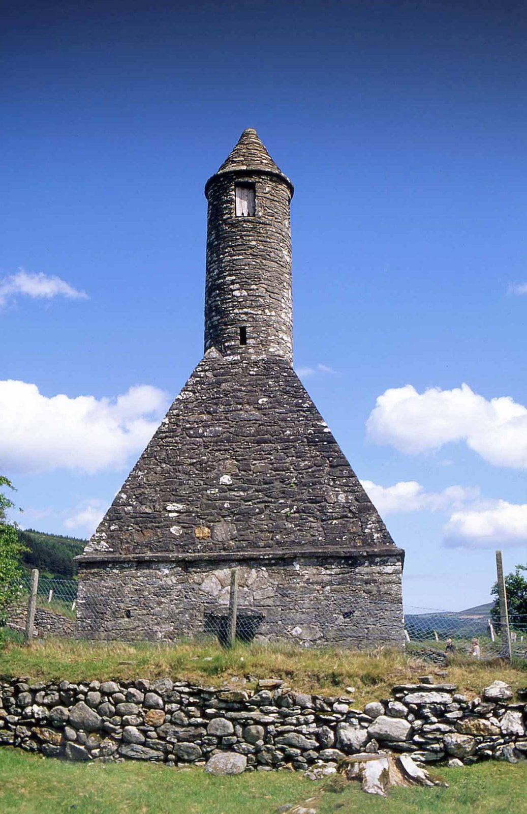 The round tower at Glendalough, a conical dry-stone tower above a field wall